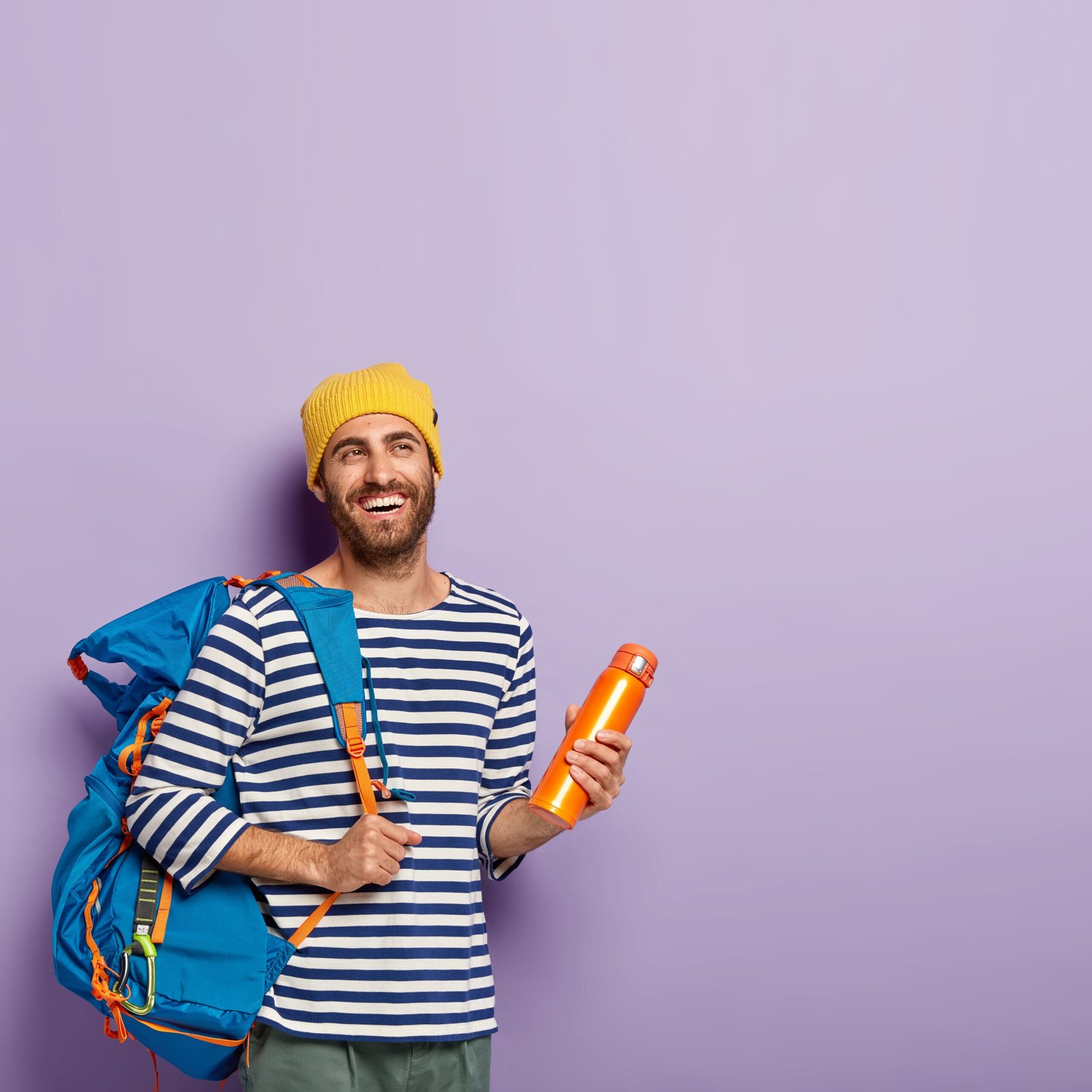 vertical shot happy unshaven male backpacker carries big tourist rucksack holds flask isolated violet wall free space people tourism scaled